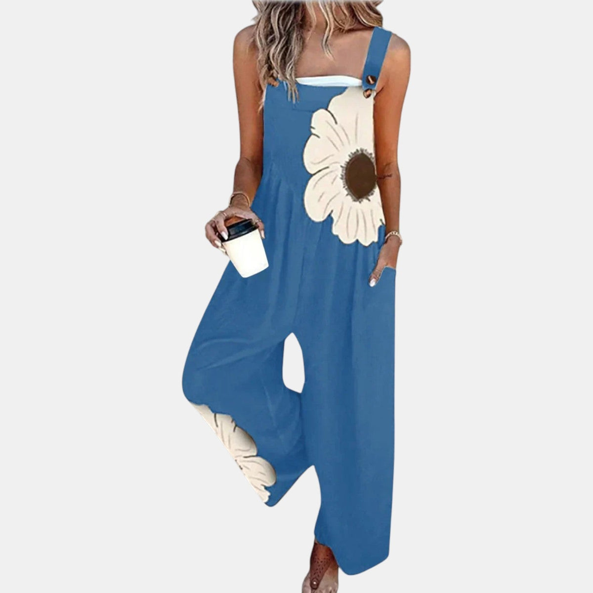 Blaue Latzhose mit großer cremefarbener Blüte vorn und am Hosenbein, Model mit Kaffeebecher 6