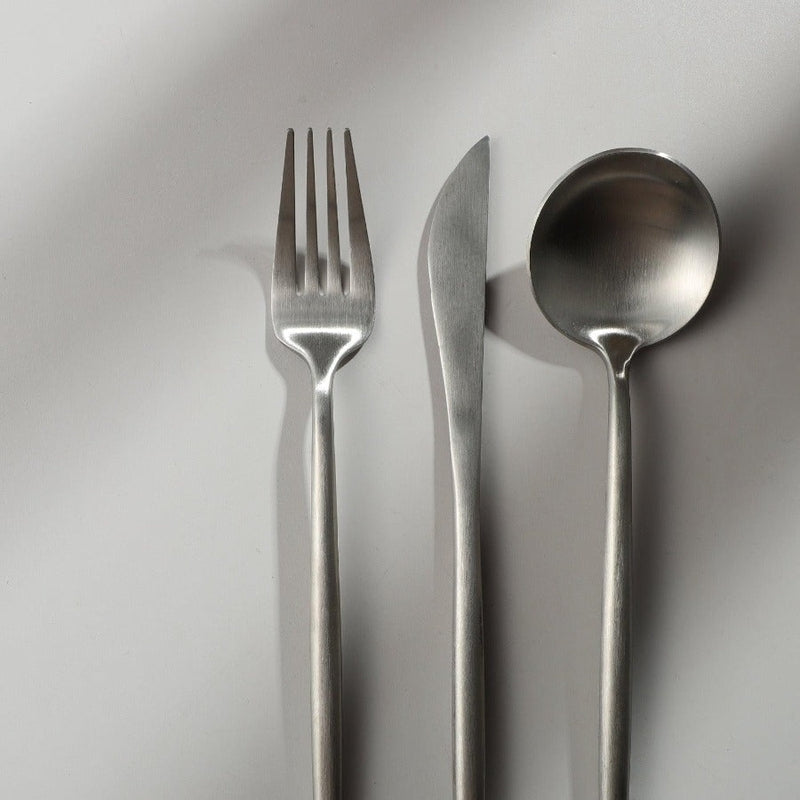 Minimalistisches Besteckset aus Edelstahl, bestehend aus Gabel, Messer und Löffel auf weißem Hintergrund.