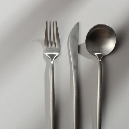 Minimalistisches Besteckset aus Edelstahl, bestehend aus Gabel, Messer und Löffel auf weißem Hintergrund.
