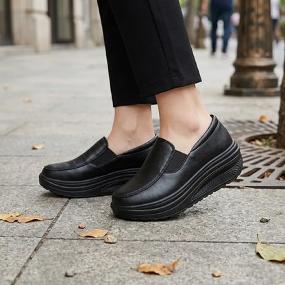 Schwarze Slipper an den Füßen einer Frau mit schwarzer Hose auf einem Gehweg mit Herbstlaub 2