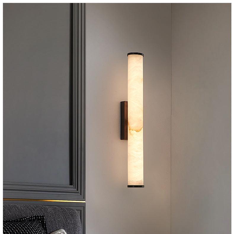 Wandlampe mit marmoriertem Zylinder und schwarzen Kappen an grauer Wand in einer Zimmerecke, links eine dunkle Wandverkleidung und ein Sofa. 13