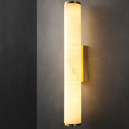 Detailaufnahme der leuchtenden Wandlampe mit geschichtetem Marmorzylinder, goldfarbenen Endkappen und Wandhalterung an dunkler Wand. 17