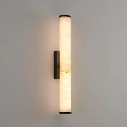 Freigestellte Ansicht der Wandlampe mit leuchtendem marmoriertem Zylinder, dunklen Endkappen und schmaler dunkler Wandhalterung an hellgrauer Wand. 19