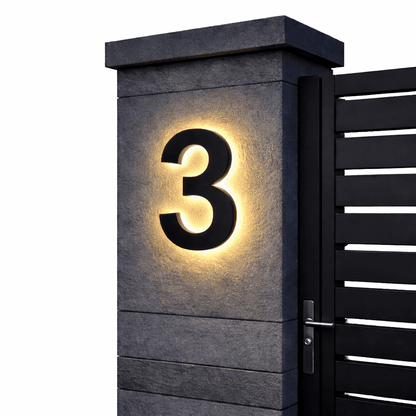 Schwarze Ziffer 3 mit warmem Hintergrundlicht an einem grauen Steinpfeiler vor schwarzem Lamellentor, freigestellt. 9