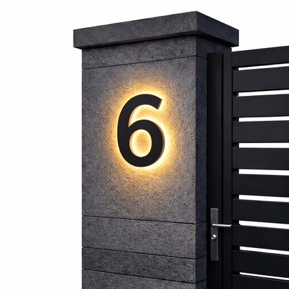 Schwarze Ziffer 6 mit warmem Hintergrundlicht an einem grauen Steinpfeiler vor schwarzem Lamellentor, freigestellt. 12