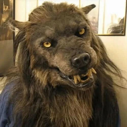 Person trägt die braune pelzige Werwolfmaske mit gelben Augen und sichtbaren Reißzähnen, leicht schräg fotografiert vor einer hellen Wand. 1