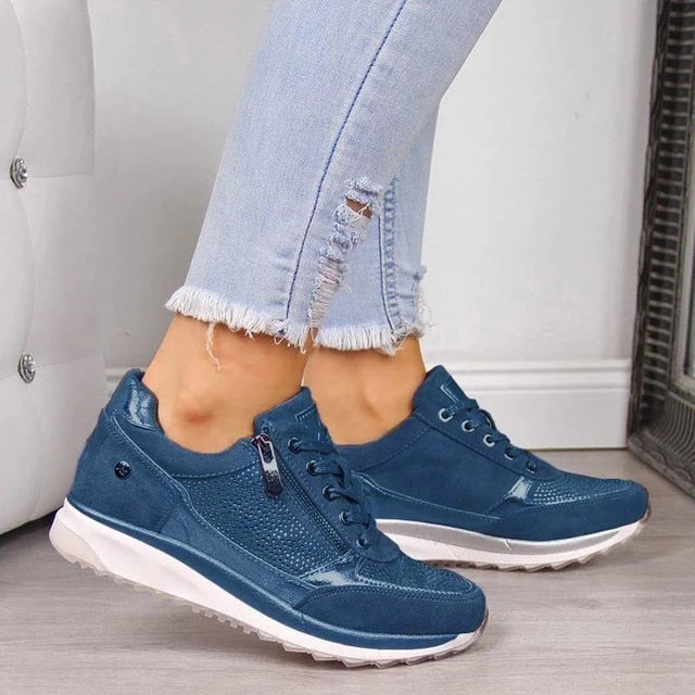 Blaue Sneaker mit seitlichem Reißverschluss, Schnürung und weißer Sohle, getragen zu hellblauer Jeans mit zerrissenem Detail. 5
