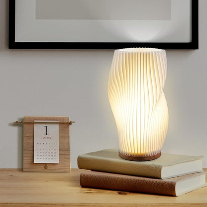Moderne Tischlampe aus Papier, weiß, wellenförmig, auf Holztisch neben Kalender und Büchern.