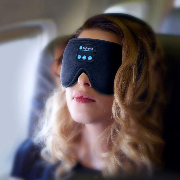 Frau mit schwarzer Bluetooth-Schlafmaske im Flugzeug, kabellose Augenmaske, Entspannung.
