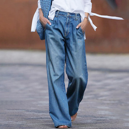 Frau in blauer, weiter Jeanshose und weißem Hemd, trägt blaue Stricktasche.