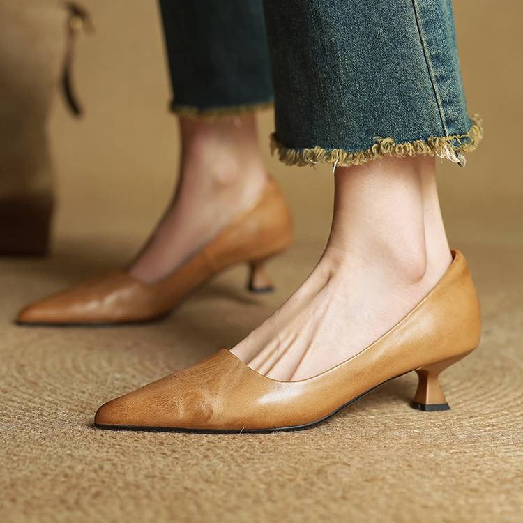 Karamellbraune Lederpumps am Fuß einer Frau, kombiniert mit Jeans mit ausgefranstem Saum, auf Bastteppich 2