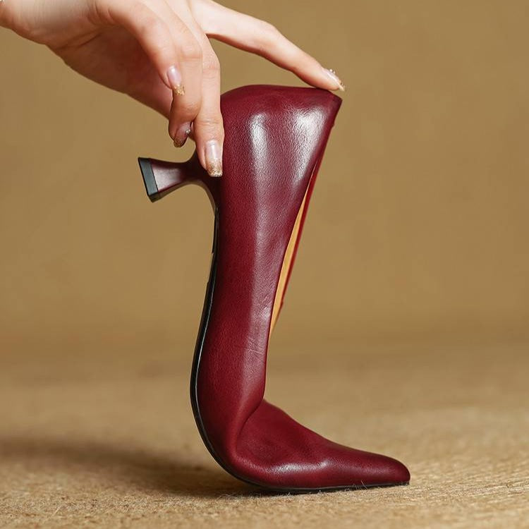 Hand hält einen weinroten Pumps aufrecht auf der Spitze, um Sohle und Absatzform zu zeigen 10