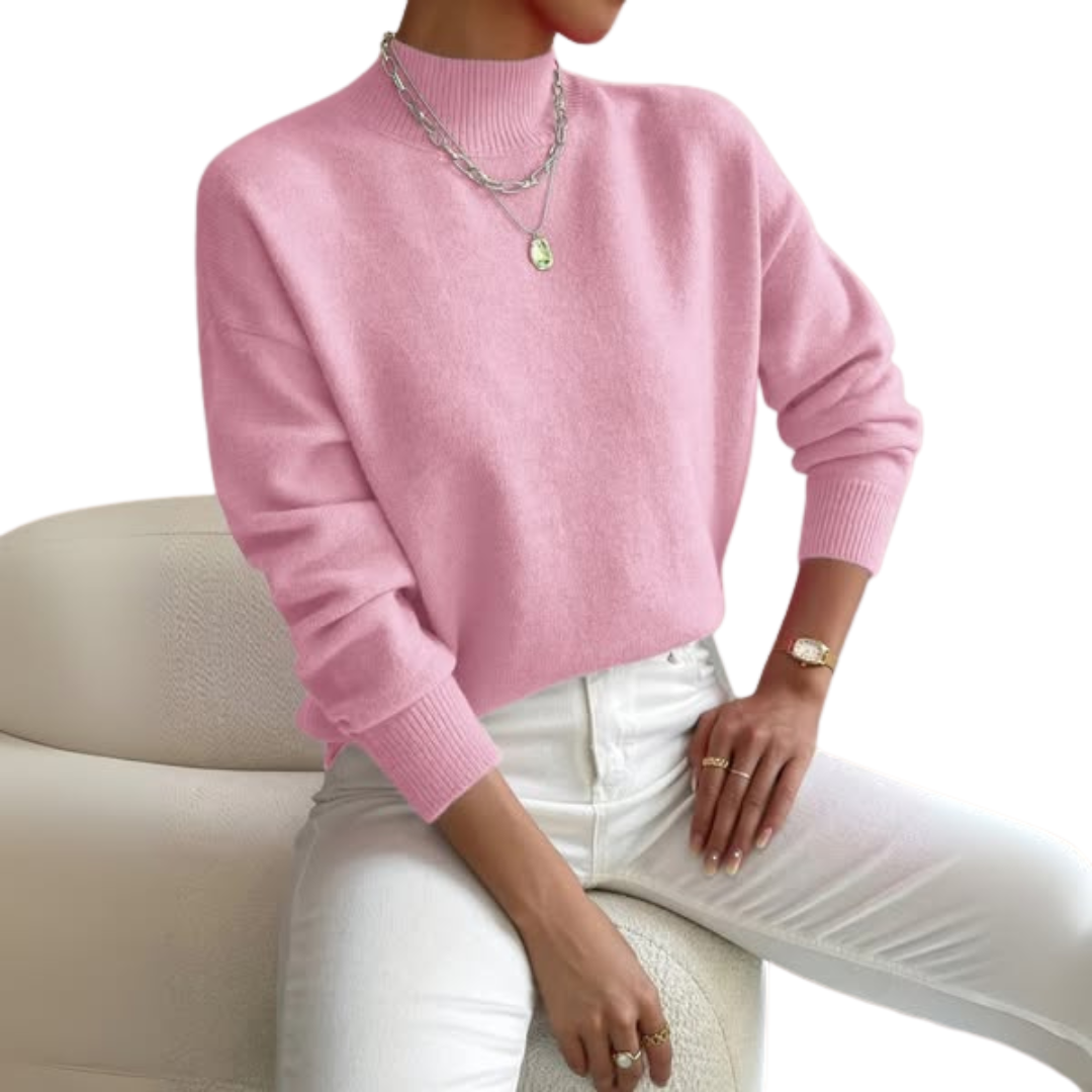 Rosa Strickpullover mit gerippten Bündchen und Stehkragen, getragen von einem Model zu weißer Jeans auf einem hellen Sessel, auf weißem Hintergrund. 1