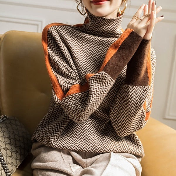 Model sitzt auf einem gelben Sessel und trägt den Fischgrät-Pullover mit orangefarbenen Streifen und breiten braunen Ärmelbündchen. 3