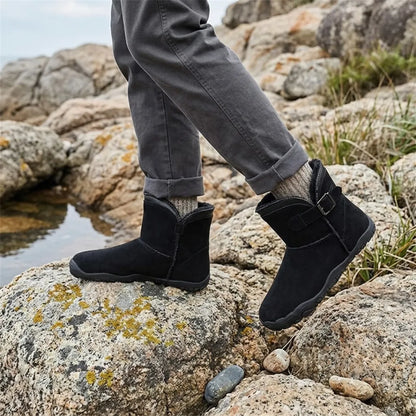 Schwarze Stiefel getragen auf mit Flechten bewachsenen Felsen am Wasser, kombiniert mit grauer Hose 11