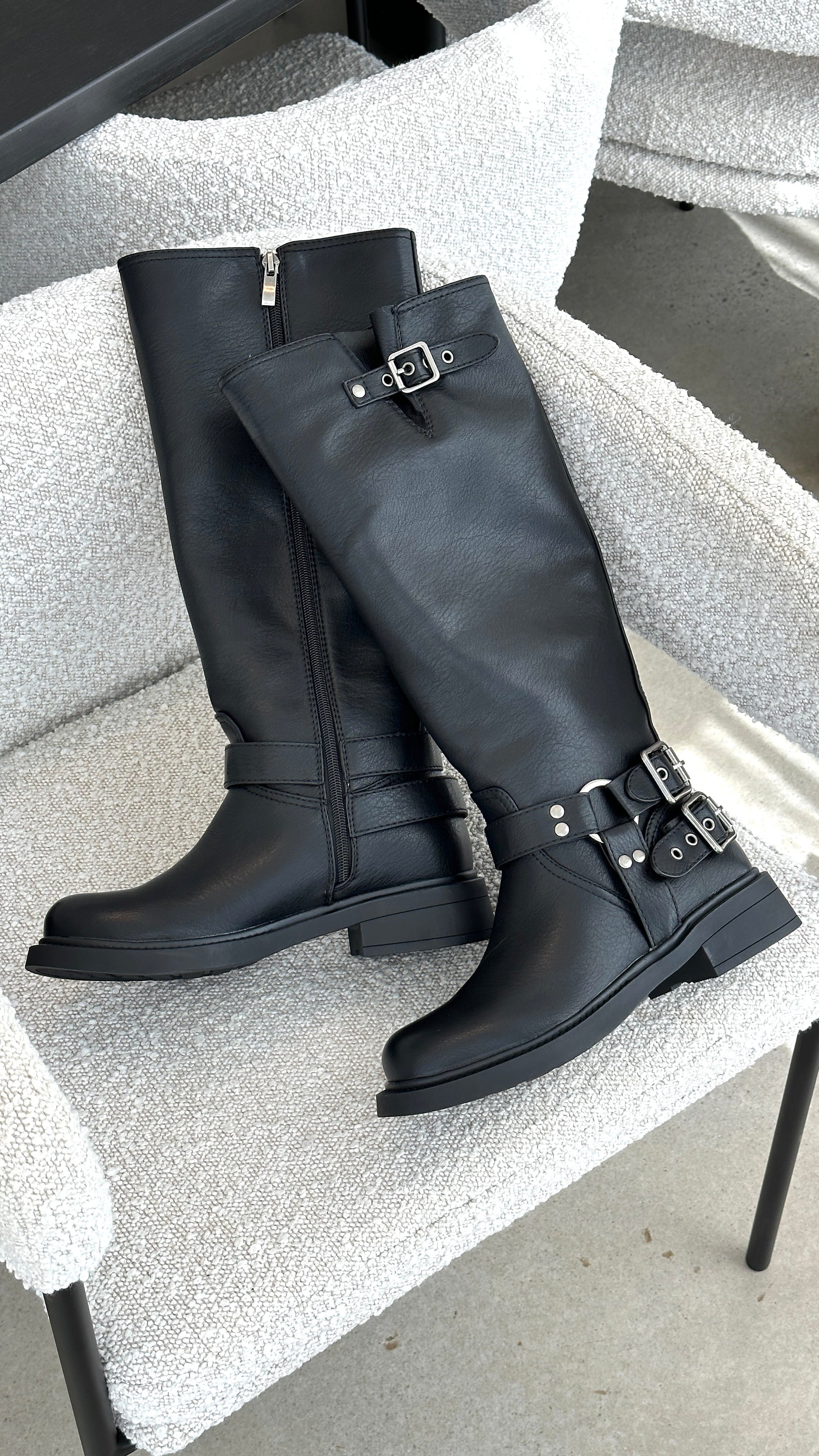 Schwarze Lederstiefel mit Schnallen auf einem weißen Sessel, modisch und elegant.
