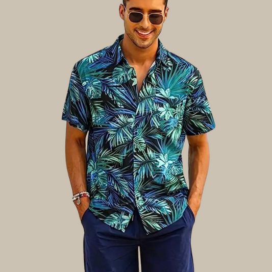 Mann in blauem Hawaiihemd mit tropischem Muster, lächelnd, trägt Sonnenbrille.