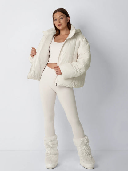 Ganzkörperansicht in Creme: Model hält die offene Jacke mit sichtbarem Fleecefutter, dazu Leggings und Pelzstiefel 2
