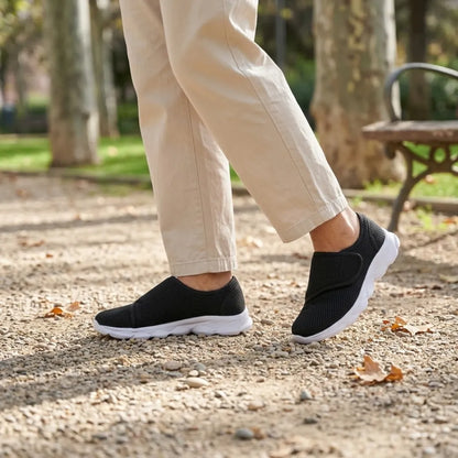 Person in beigen Hosen geht im Park und trägt die schwarzen Klettschuhe mit weißer Sohle auf Kiesweg. 20