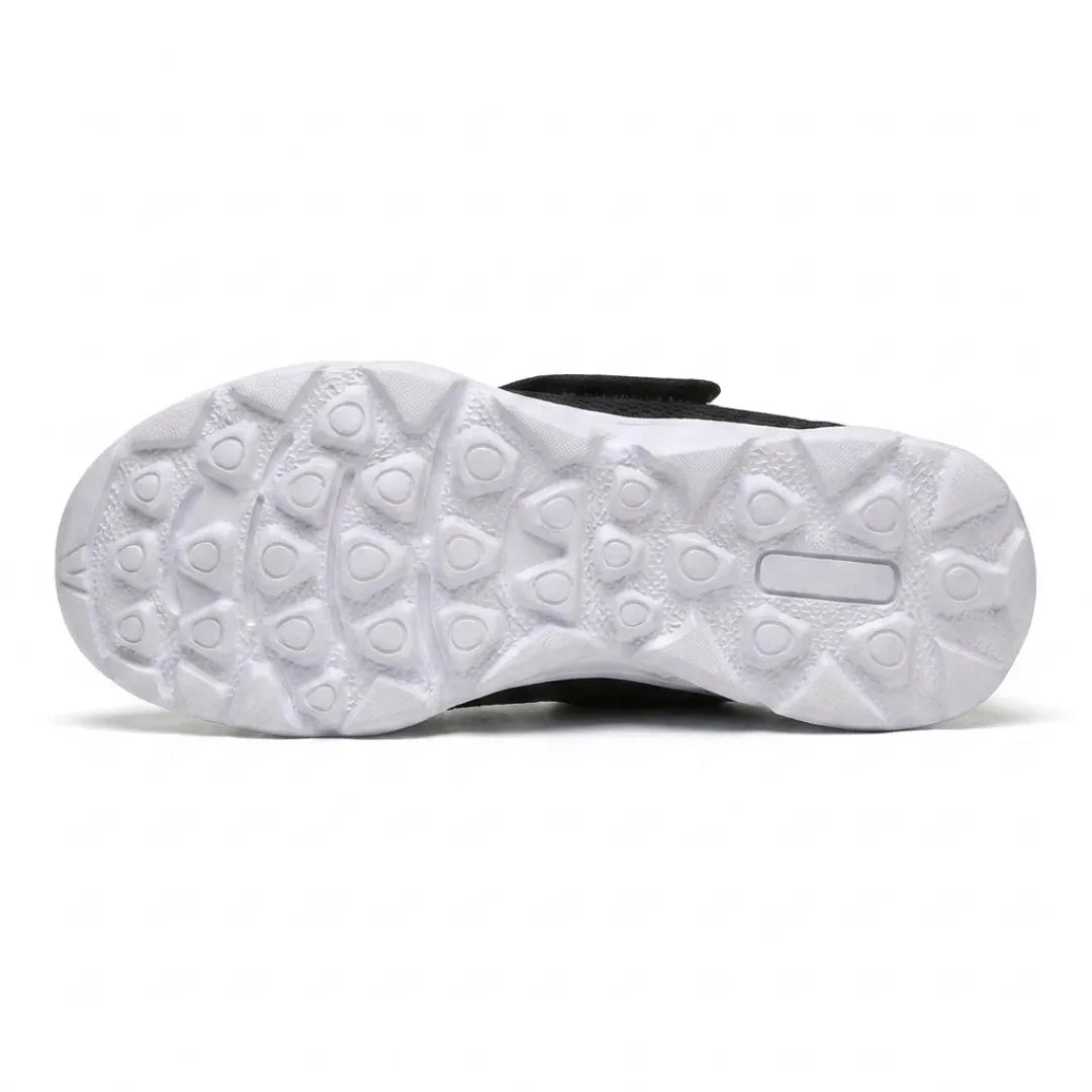 Weiße Laufsohle von unten mit Profil aus dreieckigen Noppen für rutschfesten Halt, im Hintergrund der schwarze Schuh mit Klettband. 27