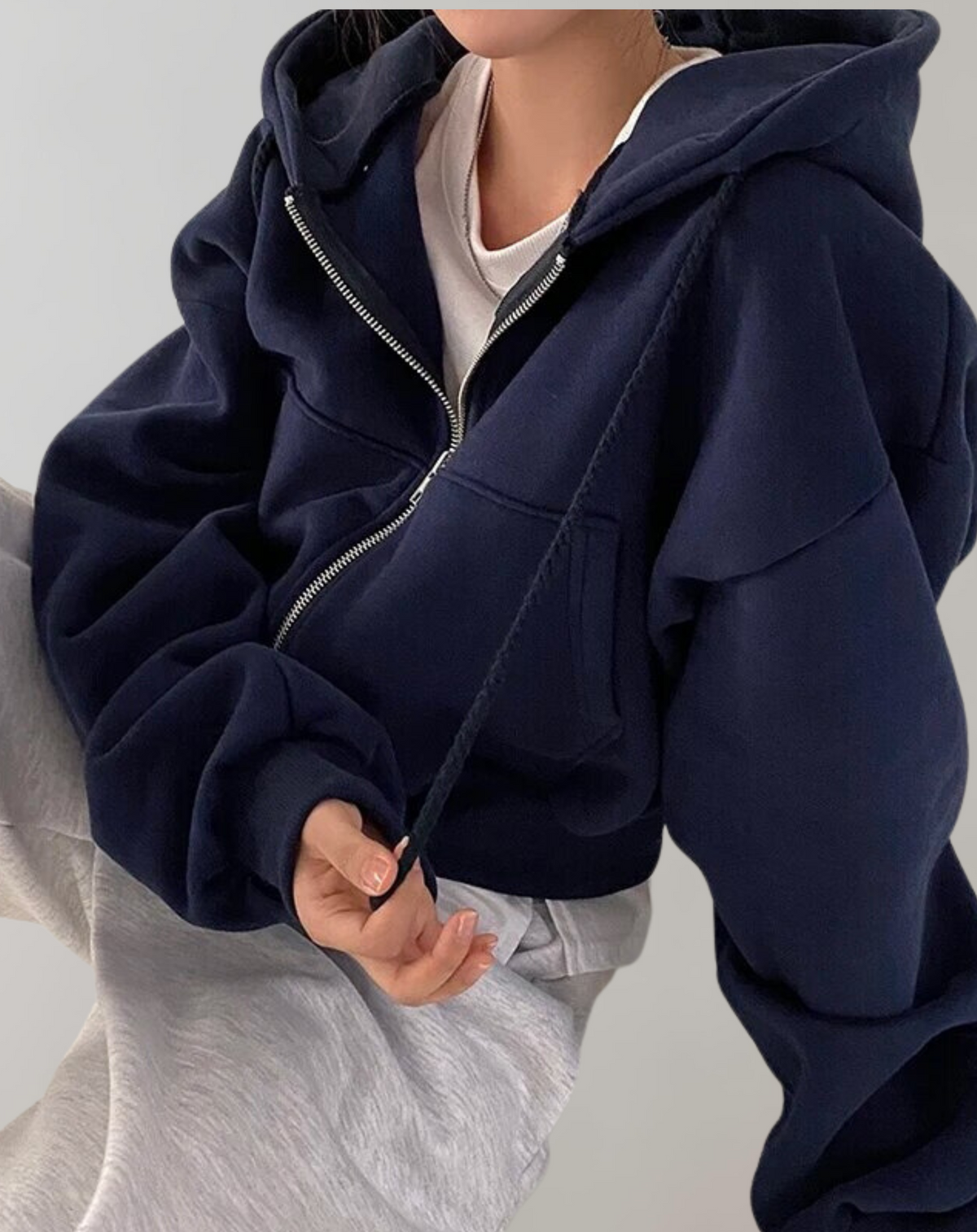 Dunkelblauer Hoodie mit geöffnetem Reißverschluss und Kordel in der Hand, getragen über hellem Shirt und grauer Hose. 3