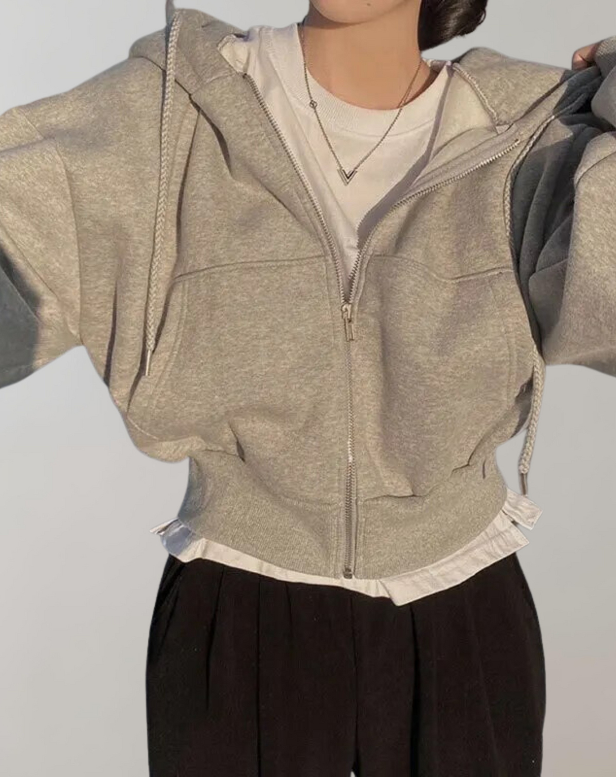 Grau melierter Hoodie mit Reißverschluss und Rippbündchen, darunter ein weißes Shirt mit sichtbarem Saum, dazu eine schwarze Stoffhose. 5