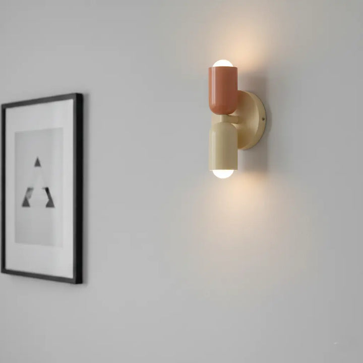 Eingeschaltete Wandleuchte in Terrakotta und Creme an grauer Wand, daneben ein schwarz gerahmtes Bild; Licht strahlt nach oben und unten. 4