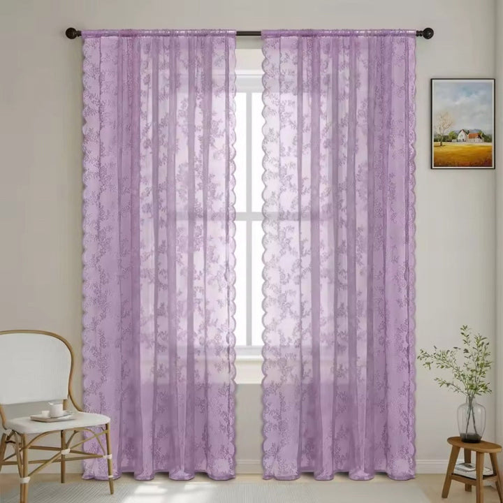 Zwei fliederfarbene Schals mit Blumenmuster und gewellter Kante an dunkler Stange vor einem hellen Fenster in einem Wohnraum. 10