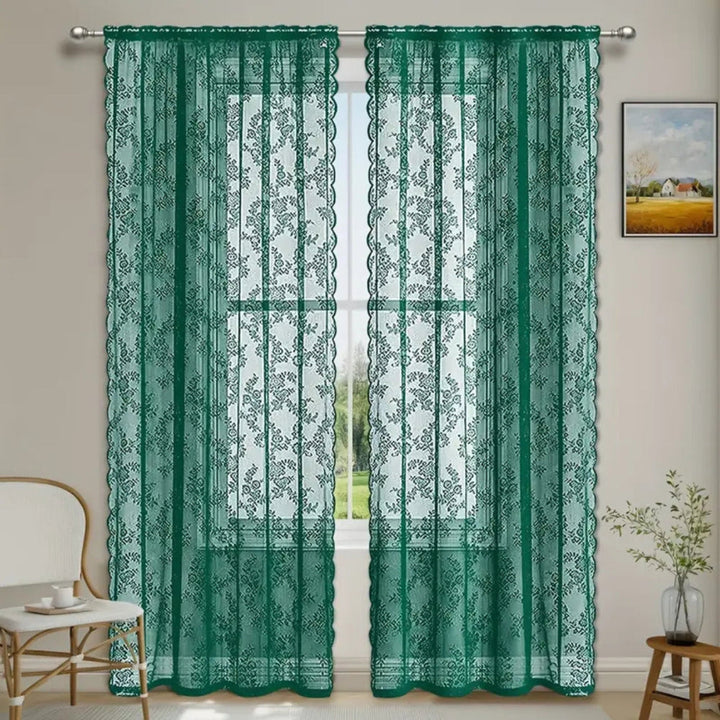 Zwei grüne, transparente Schals mit Blumenmuster an einer Stange vor einem Fenster mit Blick ins Grüne, daneben Stuhl und Pflanze. 5