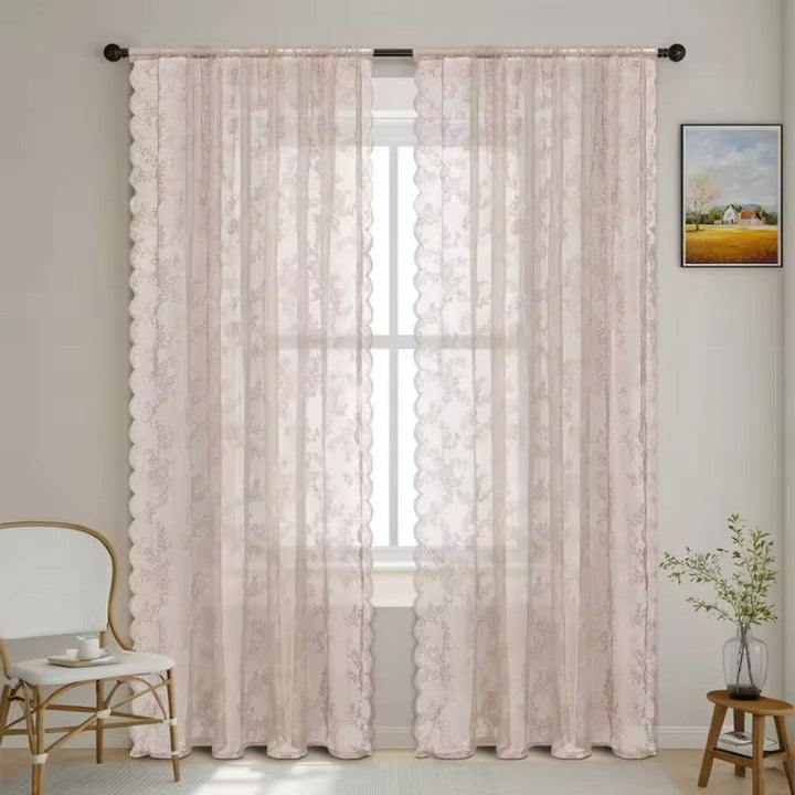 Zwei rosé-beige Schals mit feinem Blumenmuster und Wellenrand an dunkler Stange vor einem Fenster, daneben Stuhl, Bild und Pflanze. 9