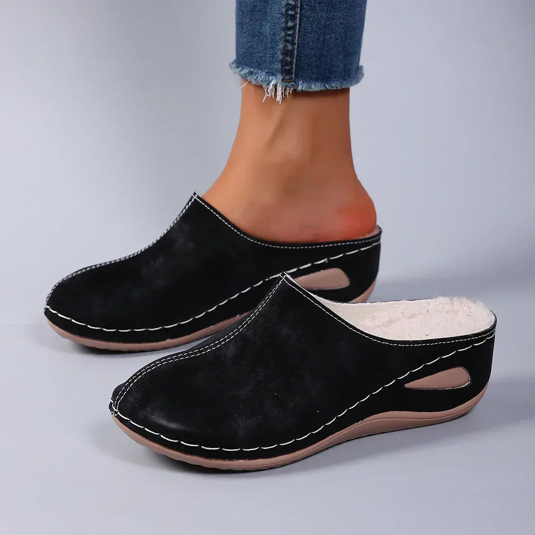 Schwarze Pantoffeln mit heller Sohle und sichtbarem Fleecerand, von einer Person in Jeans getragen, Seitenansicht. 2