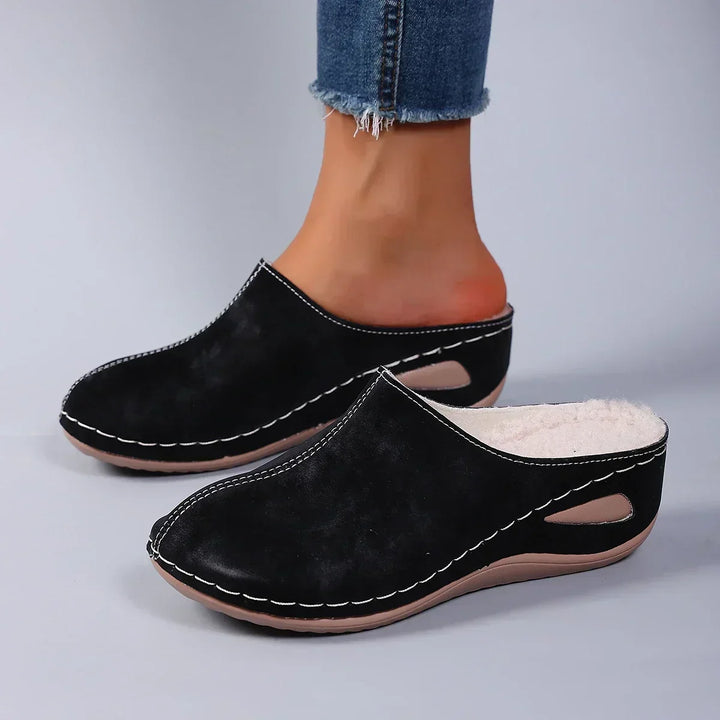Schwarze Pantoffeln mit heller Sohle und sichtbarem Fleecerand, von einer Person in Jeans getragen, Seitenansicht. 2