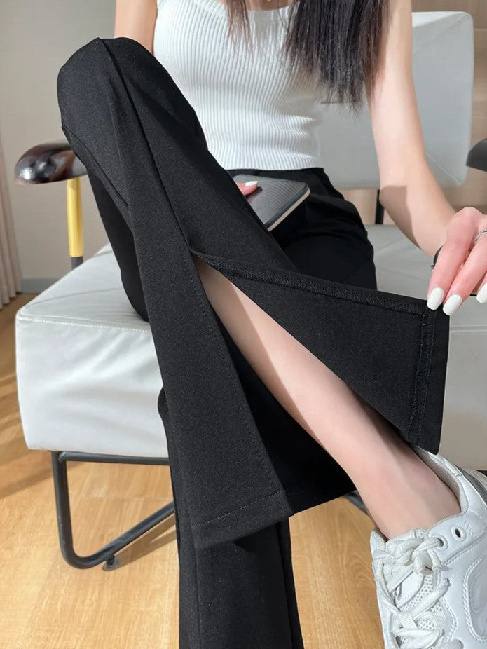 Frau in schwarzer Schlaghose mit Schlitz, weißem Top und Sneakers auf Stuhl sitzend.