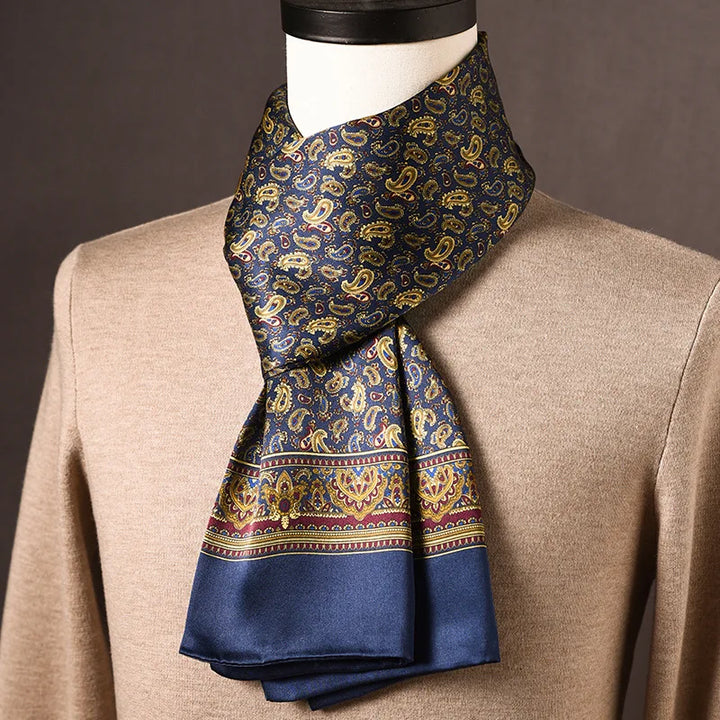 Marineblauer Seidenschal mit goldenem Paisleymuster und weinroter Zierbordüre, auf einer Büste mit beigem Pullover drapiert. 12