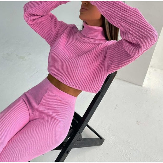 Frau in rosa Strick-Zweiteiler, Rollkragenpullover und Hose, sitzt auf schwarzem Stuhl.