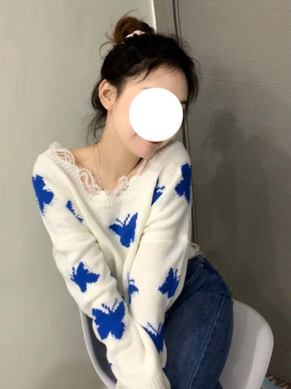 Frau in weißem Pullover mit blauen Schmetterlingen, sitzt auf Stuhl, lässige Mode.