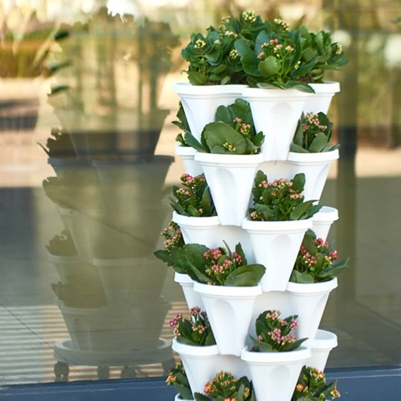 Vertikaler Pflanzenturm aus weißem Kunststoff mit grünen Pflanzen und rosa Blüten, ideal für Balkon.