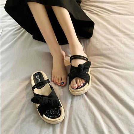 Schwarze Damen-Sandalen mit Schleife, flach, Sommermode, bequem, auf Bett liegend.