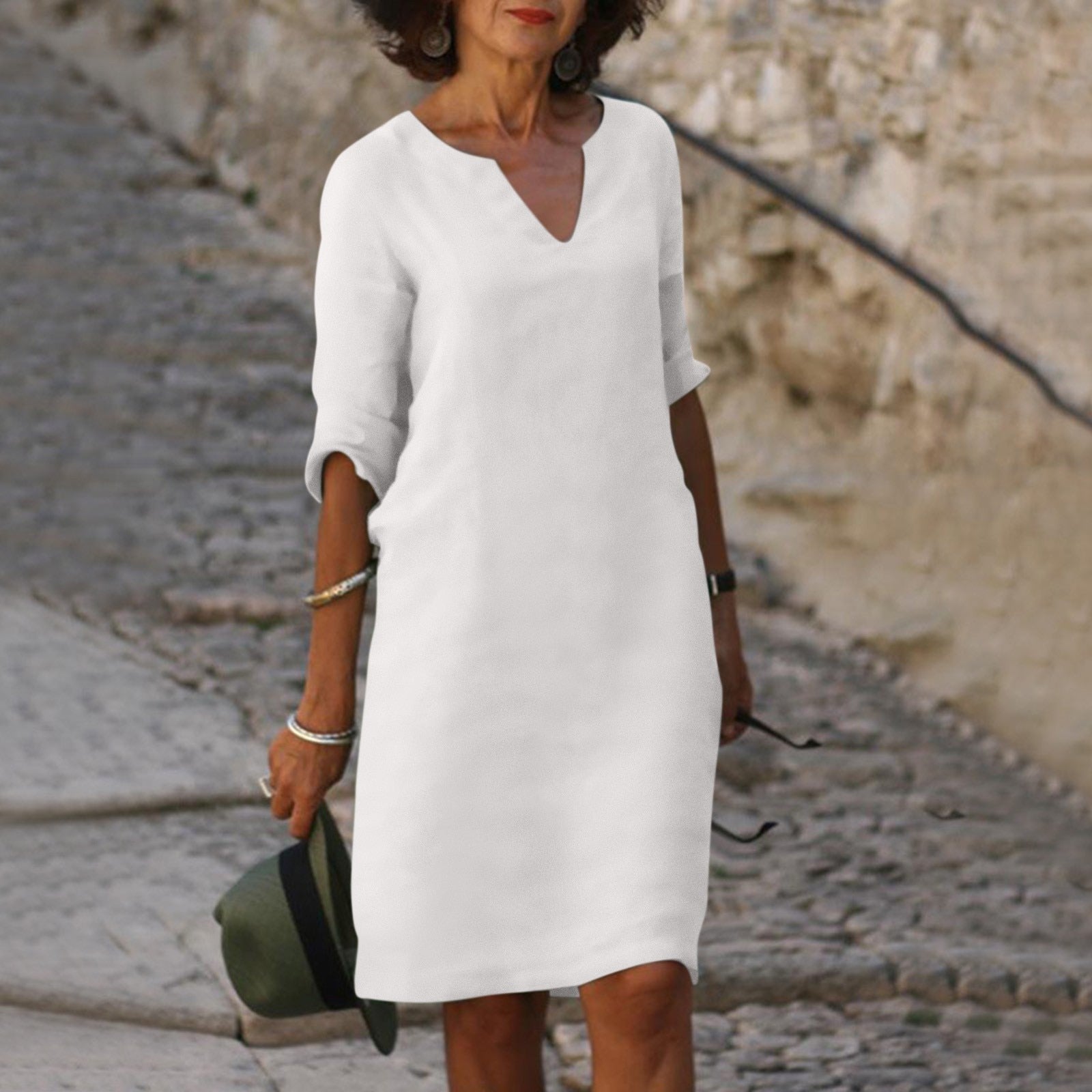 Weiße Damen-Leinenkleid, V-Ausschnitt, knielang, lässig, Sommermode, Spaziergang auf Kopfsteinpflaster.