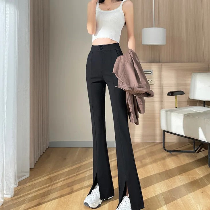 Frau in schwarzer Schlaghose und weißem Top, hält braune Jacke, moderne Inneneinrichtung.