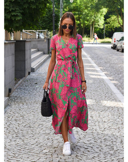Frau in rosa-grünem Blumenkleid mit Sneakers und schwarzer Tasche auf gepflasterter Straße.