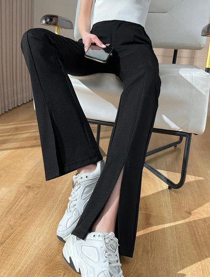 Frau in schwarzer Hose mit Schlitz, weiße Sneaker, Smartphone, moderne Inneneinrichtung.