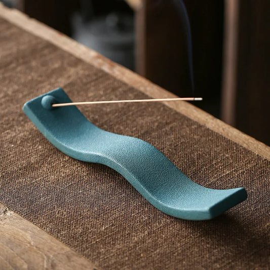 Grüner Keramik-Räucherstäbchenhalter auf Holztisch, wellenförmig, modern, dekorativ.