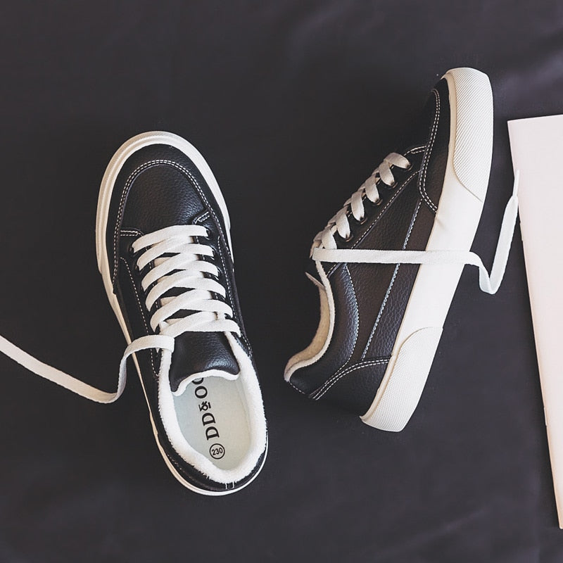 Schwarze Leder-Sneaker mit weißen Schnürsenkeln auf dunklem Hintergrund, modisch und bequem.