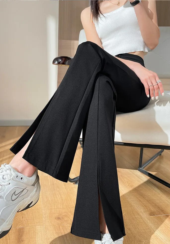 Frau in schwarzer Schlaghose und weißem Top, sitzt auf Stuhl, trägt weiße Sneakers.