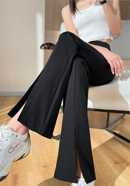 Frau in schwarzer Schlaghose und weißem Top, sitzt auf Stuhl, trägt weiße Sneakers.