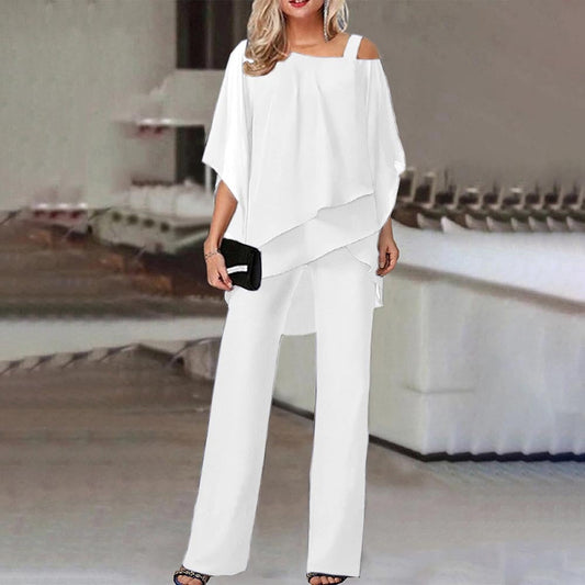 Frau in weißem, schulterfreiem Hosenanzug mit schwarzer Clutch in modernem Innenraum.