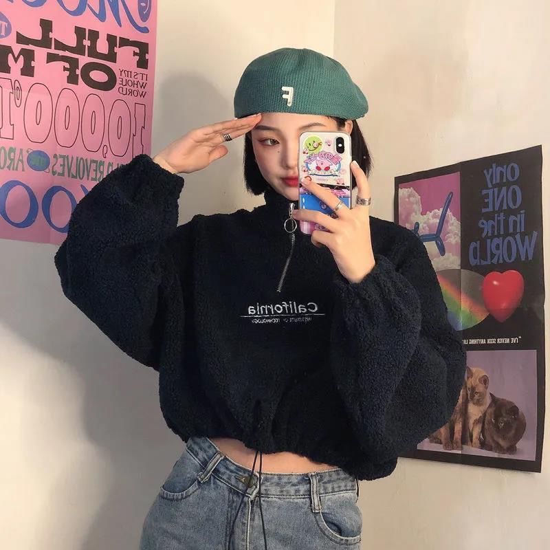 Frau in schwarzem Teddyfleece-Pullover, grüner Mütze, Jeans, Selfie im Spiegel.