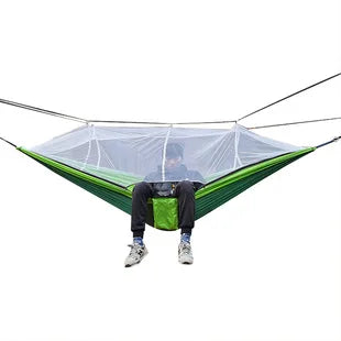Grüne Hängematte mit Moskitonetz, Outdoor-Camping, Person sitzend, isoliert auf weißem Hintergrund.