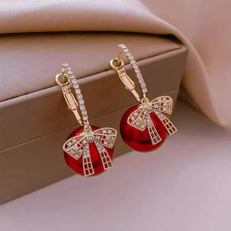 Goldene Ohrringe mit rotem Anhänger und Schleife, funkelnde Kristalle, eleganter Schmuck.